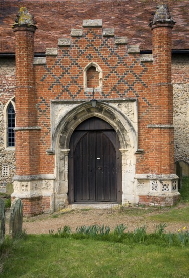 Tudor red brick porch set against more ancient building. St Peter's church, Charsfield Suffolk, England, UK
