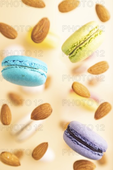 Multicolored flying macaroons and almonds frozen in the air on blurred beige background. top view, flat lay, close up. Breakfast, morning, concept