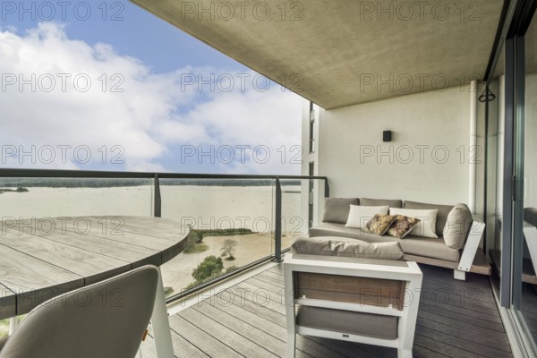 A stylish balcony featuring a cozy seating area overlooking a serene water view and bright sky, ideal for relaxation and leisure