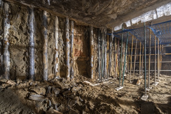Underground construction site showing exposed dirt walls and temporary supports. The area is dimly lit, emphasizing the rugged and unfinished surroundings