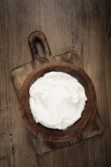 Sour cream in a wooden bowl, on a wooden table, top view, close-up, no people