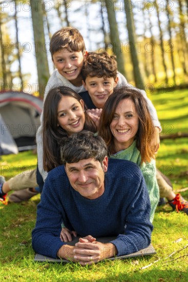 Caucasian family having fun together lying on the forest one on top of each other next to camping tent