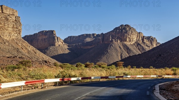 A road with a bend winds its way through impressive mountain scenery in a barren desert landscape under a bright sun, A drive through the mountain landscape of the Sahara in Algeria