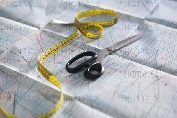 Scissors and a yellow measuring tape rest on detailed sewing pattern paper. This setup captures the essence of a creative sewing workshop environment