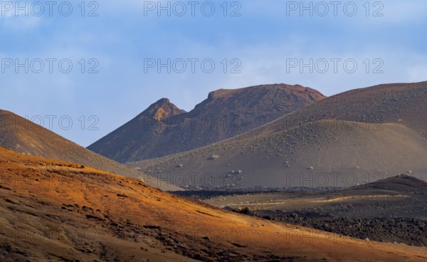 Scenic view of Timanfaya National Park's dramatic volcanic landscape with sunlit hills and rugged mountains in Lanzarote, Canary Islands, Spain