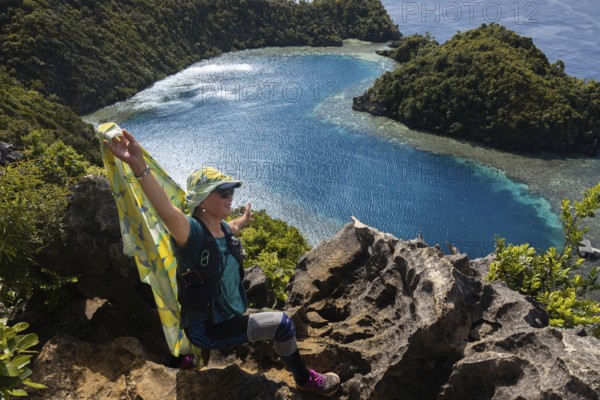 A traveler embraces nature on a cliff overlooking the stunning blue waters and lush greenery of Raja Ampat Archipelago, Indonesia, ideal for ecotourism