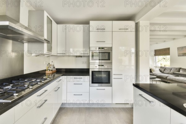 A contemporary kitchen featuring sleek stainless steel appliances, glossy white cabinets, and a black counter top, creating a stylish and functional cooking space