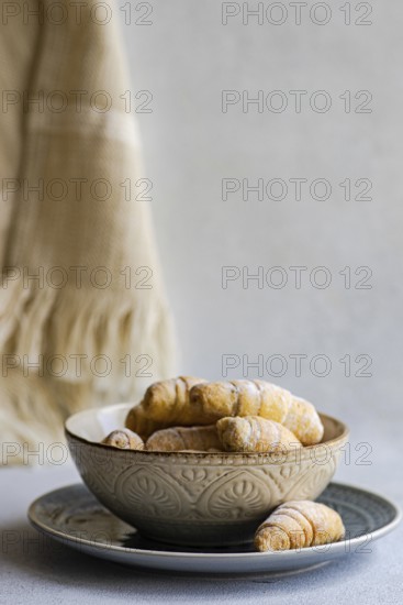 A decorative bowl filled with freshly baked homemade pastries, placed on a plate. The pastries are lightly dusted with sugar, creating an inviting and warm presentation