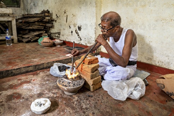 A man blows into a coal-fired pool with a concentrated face, a man burns sapphires in a small stove in the town of Ratnapura in Sri Lanka