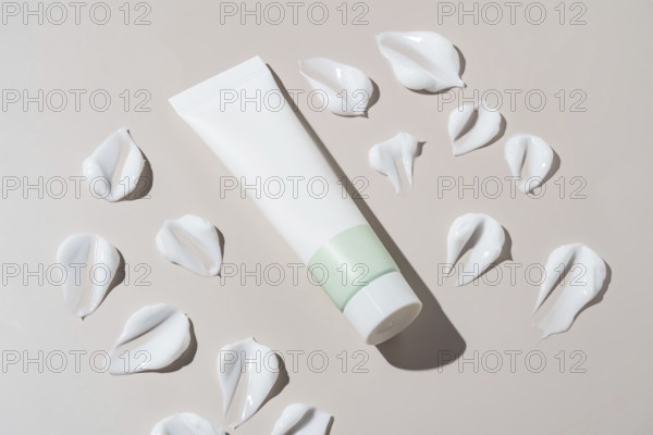 An elegant cosmetics container with a minimalist design appears next to artistic cream stains on a neutral background. The textures add depth and elegance to the composition