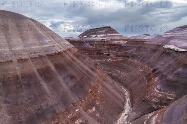 A stunning drone photograph capturing the layered geological formations unique to Hanksville, Utah, showcasing a spectrum of earthen colors under a moody sky