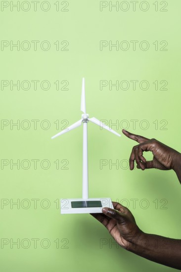 Close-up of a hand holding a small wind turbine model, symbolizing renewable energy innovation, set against a vibrant green background, highlighting sustainability