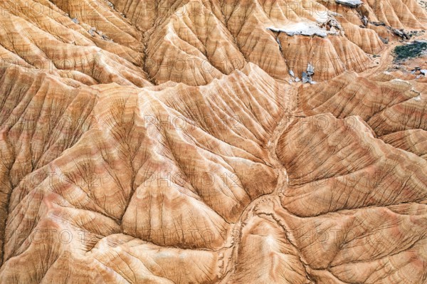 Aerial shot captures a striking desert landscape with rugged, eroded hills and vivid geological patterns The natural textures create an intricate and mesmerizing view