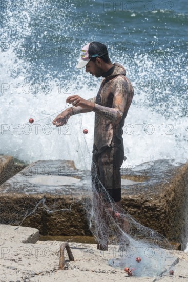 Alexandria, Egypt. June 26th 2024. A young Egyptian fisherman wearing a wetsuit arranges his net on the Mediterranean Sea front of Alexandria, second largest city in Egypt