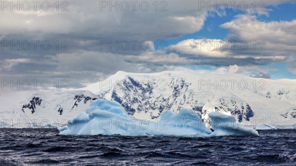 Icebergs floating in undulating water against a backdrop of snow-capped mountains under a dramatic sky, icebergs in the landscape of the Southern Ocean in Antarctica