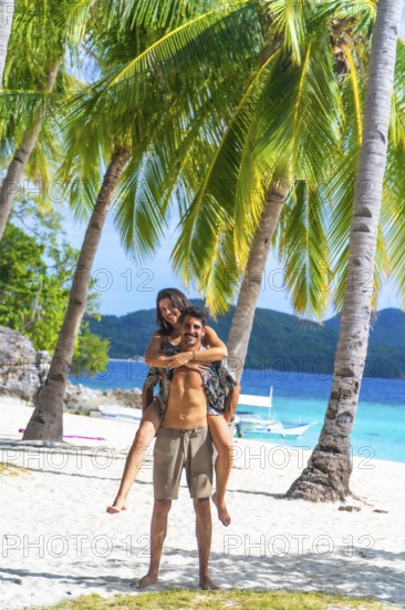 Tourists having fun on a beautiful white sand beach with turquoise water and palm trees on malcapuya island, coron, philippines