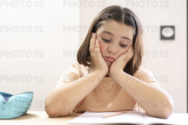 A young girl sits at a desk, appearing stressed and overwhelmed with her homework. Her head rests on her hands, and a pencil case sits close by, evoking school life challenges