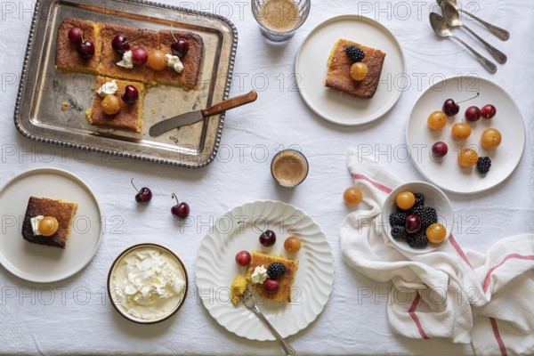 Top view of a sweet dessert table featuring slices of cake embellished with cherries, blackberries, and whipped cream, accompanied by cups of coffee. A rustic setting completes the homey mood, ideal for a leisurely afternoon snack