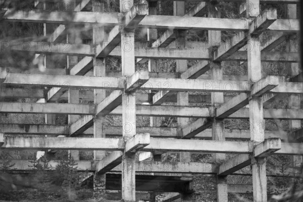 Black and white photo showcasing the intricate geometric pattern of concrete beams and pillars in an unfinished, abandoned building, depicting decay and urban exploration