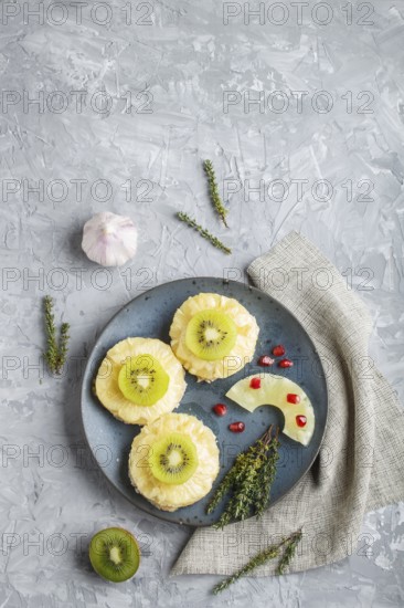 Pieces of baked pork with pineapple, cheese and kiwi on gray background, top view, copy space