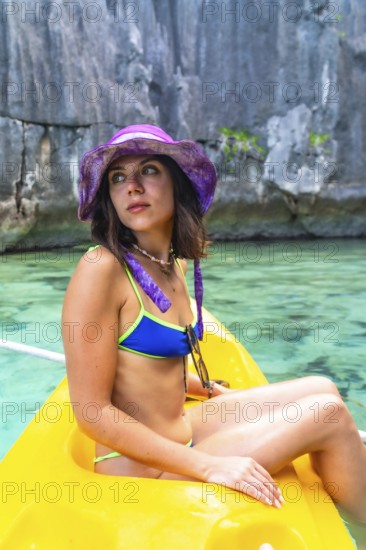 Young woman wearing a bikini and a purple hat enjoys kayaking in the crystal clear waters of twin lagoon, coron island, philippines