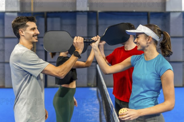 Four friends on a blue pickleball court paddle to paddle over the net, smiling and high fiving after a friendly match, celebrating teamwork, fitness, and fun