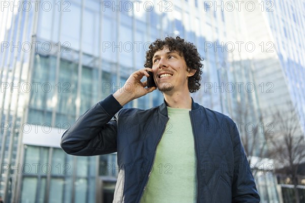 A businessman holds a phone to his ear while walking outside a modern glass building. The image captures a moment of connection and communication in a professional setting