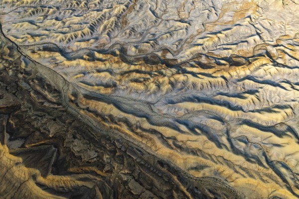 Aerial view showcasing the unique textures of a golden sandstone desert in Utah, USA. The sunlight casts dynamic shadows, highlighting the intricate landscape patterns