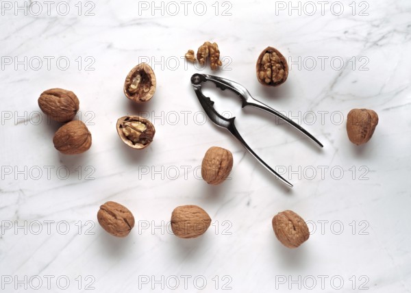 A scattered arrangement of whole and cracked walnuts with a metal nutcracker on a smooth marble surface, lit by natural light to highlight textures and shadows