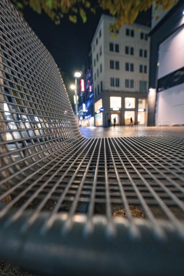 Night shot of a modern bank in a city street with illuminated shops in the background, Stuttgart, Germany