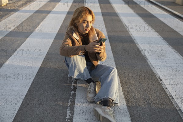 A Mixed-race woman sits quietly at a crosswalk, absorbed in her smartphone Natural light enhances her relaxed and contemplative mood in an urban setting