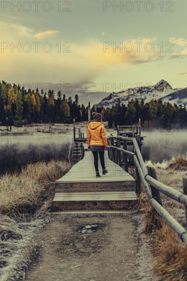 Young woman at Lake Staz near Sankt Moritz in the Engadine in Switzerland. Morning atmosphere with fog in autumn. Reflection of water