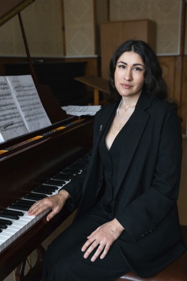 A musician in formal black attire sits beside a grand piano Sheet music is visible in the background, suggesting a rehearsal or practice session in a stylish studio