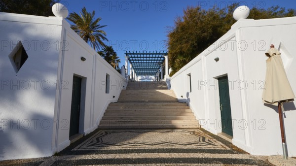 A wide staircase, flanked by white minimalist walls, leads to the top, surrounded by palm trees, Kalithea, Kallithea, thermal baths, thermal baths, bathing complex, Rhodes, Dodecanese, Greek Islands, Greece