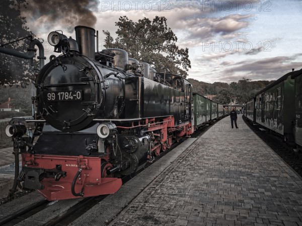 Old, historic steam locomotive in bright colors on tracks at the station in a nostalgic atmosphere, front view of speeding Roland on Rügen at sunset