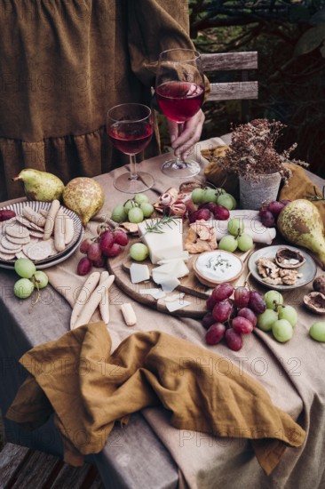 A rustic setup featuring a delicious cheese and fruit platter paired with two glasses of red wine. Grapes, pears, and a variety of cheeses create a perfect snack atmosphere