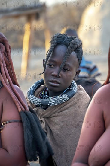 Himba girl, between Himba woman, portrait, in the morning, traditional Himba village, Kaokoveld, Kunene, Namibia