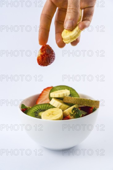 Introducing ingredients from above with a woman's hand, recipe for a fruit salad with kiwis, strawberries, bananas