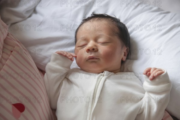 A serene newborn baby peacefully sleeps on a soft white pillow. The infant is dressed in a cozy white onesie, showcasing the beauty and tranquility of new life