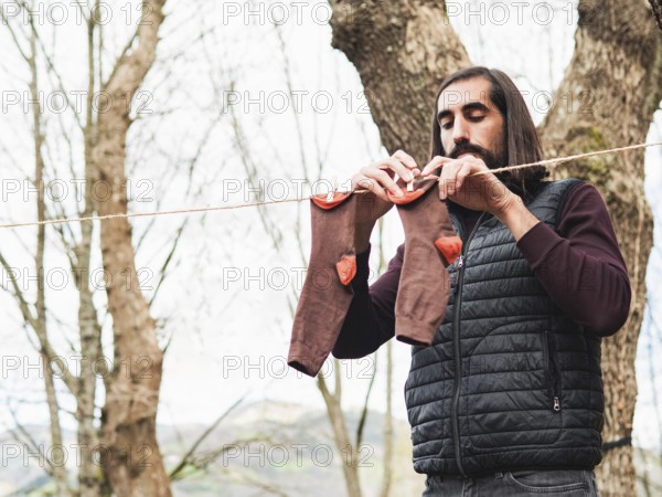 A man hangs clothes on a line in a forest, emphasizing simplicity and nature. The scene highlights harmony with the outdoors, featuring trees and serene surroundings