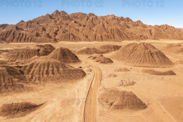 Aerial view of a vast desert landscape featuring a rugged mountain range and a winding dusty road under a clear blue sky in the argentine Puna, showcasing the beauty of arid terrains
