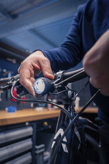 Hand adjusts the light on the bicycle handlebars in a dark blue workshop, technical focus, Waldbike Manufaktur, bicycle workshop, Calw, district of Calw, Black Forest, Germany
