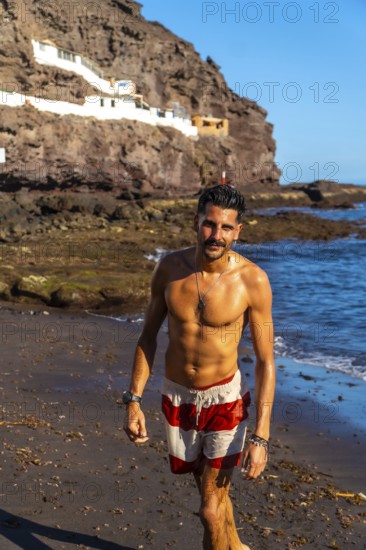 Young hispanic man walking on the beach of tufia, a coastal village of gran canaria, canary islands, spain