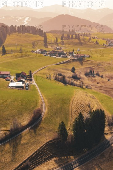 A small village is nestled in rolling hills and green meadows, surrounded by mountains, Oberreute, Allgäu, Germany