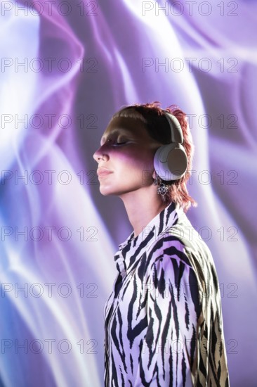 A young, trendy woman with short hair wears headphones while enjoying vibrant purple lighting. Her eyes are closed as she feels the music, embodying a modern and stylish vibe