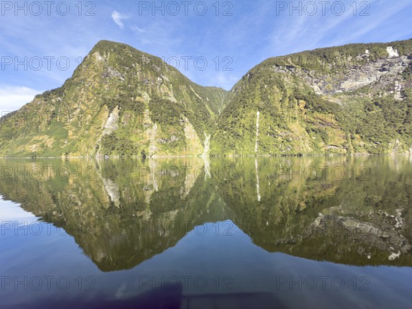 Mountains with reflections in the water against a blue sky in Doubtful Sound, South Island, New Zealand, Oceania