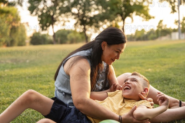 A mother lovingly embraces her son with cerebral palsy as they enjoy a sunny day in the park. They share a joyful moment together on the grass