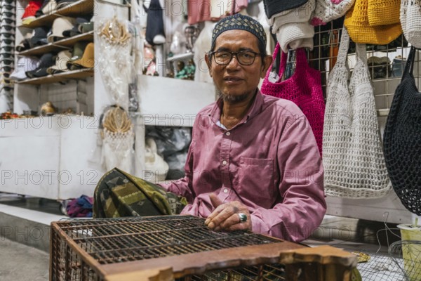 A balinese vendor in a traditional market, wearing glasses. Surrounded by various handmade items and textiles, showcasing the cultural richness and craftsmanship