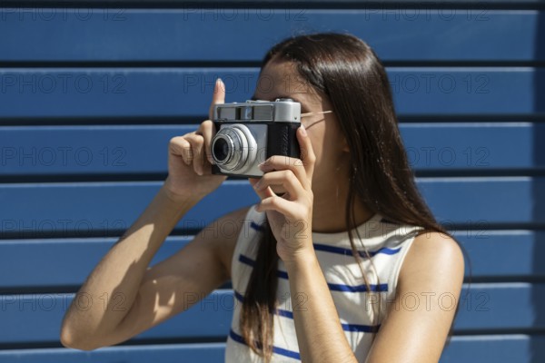 A young woman joyfully explores city life through the lens of a vintage camera, embodying the adventurous spirit of urban outdoor living on a bright, sunny day