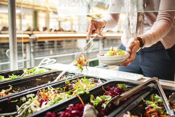 Fresh salads in a salad bar, a woman helps herself at the buffet
